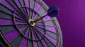 Blue dart hitting the bullseye of a purple and black dartboard