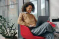 female working on laptop while sitting on a red chair in modern office space