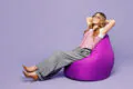 Full body business woman wearing suit vest white t-shirt glasses work in office sit in bag chair close eyes hold hands behind neck isolated on plain purple background